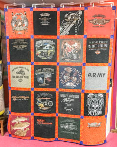 A colorful quilt made from a collection of Harley Davidson t-shirts